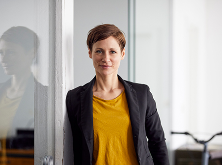 Woman in her 30's with short brown hair leaning against glass office